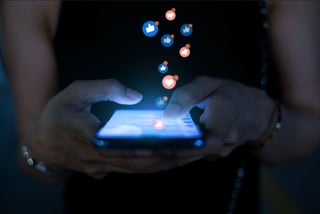 Braços de uma mulher segurando o celular com ícones de interação em redes sociais saltando da tela